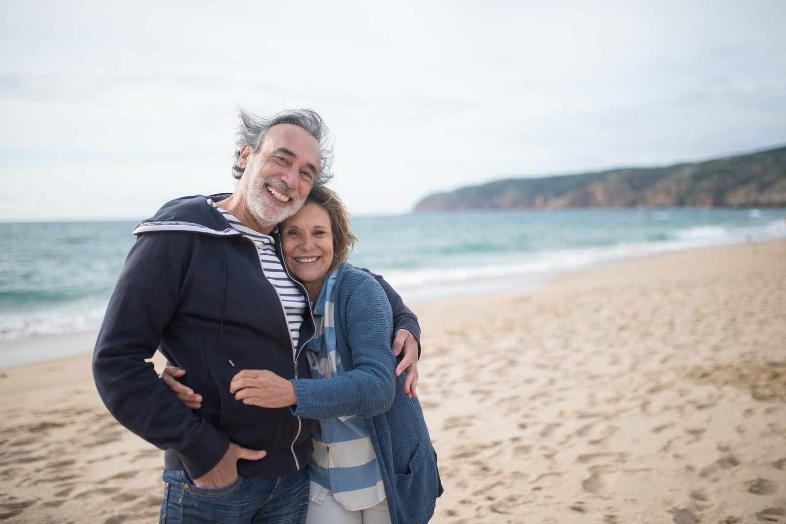 A smiling couple embracing on a beach and looking toward the camera